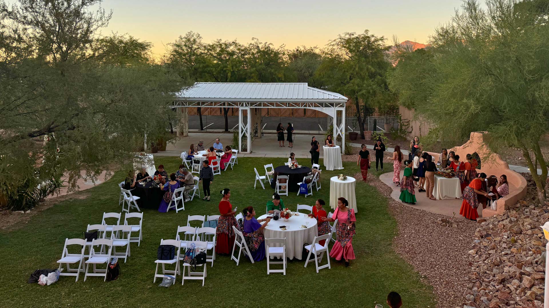 People mingle on the green lawn of Himaya Garden's outdoor area during an event. White chairs, round tables, and a large white pavilion are visible.