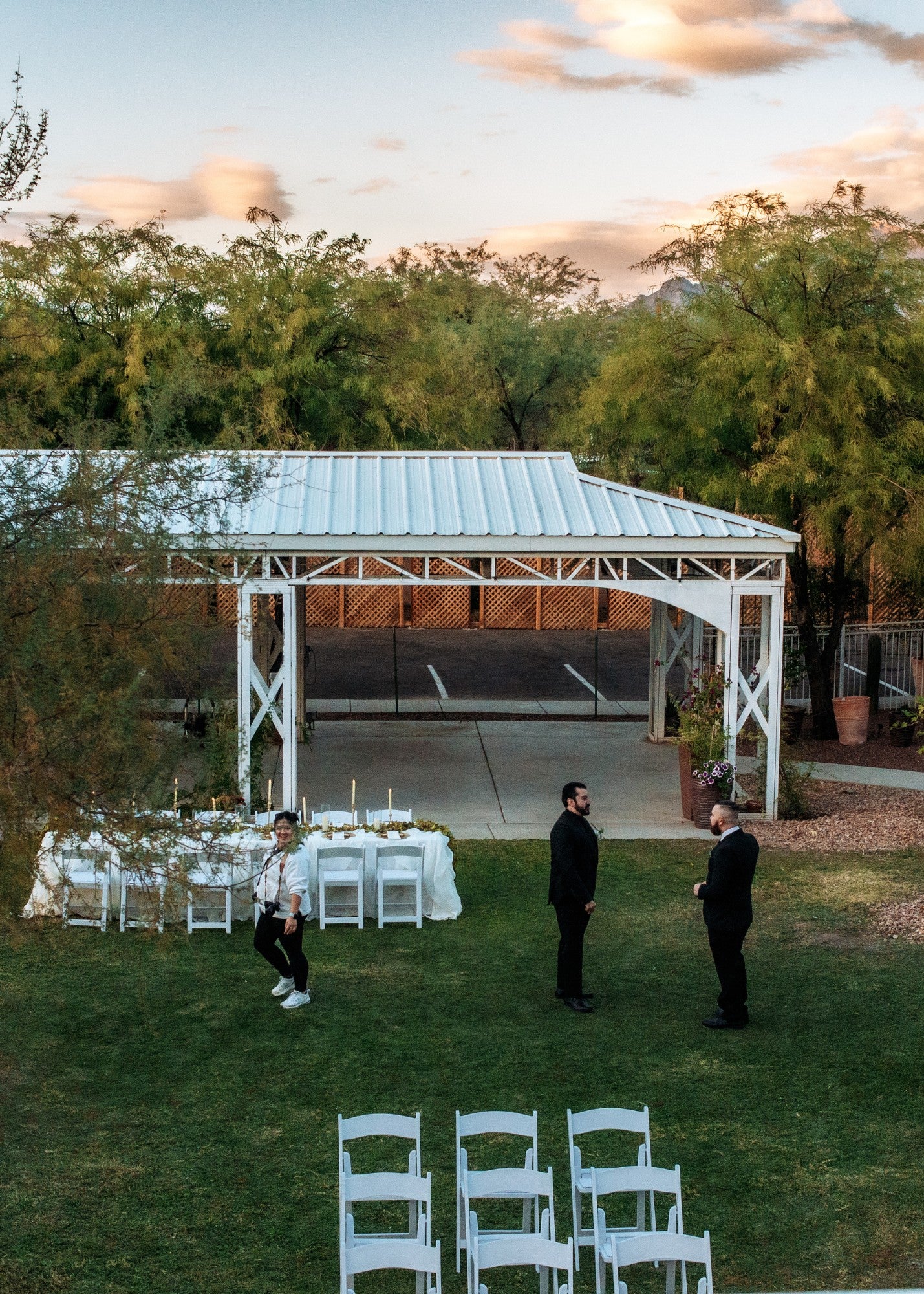 Himaya Garden aerial shot: large open outdoor event space, white chairs, aisle, trees, cloudy sky.